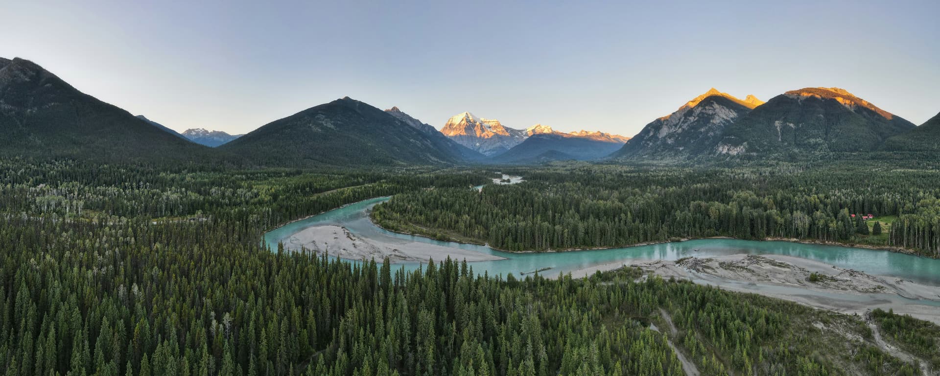Aerial view of a turquoise river winding through forest toward Mount Robson at sunrise, British Columbia
